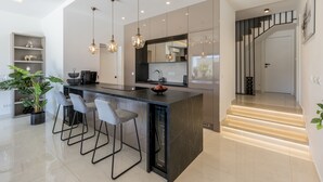 Een moderne keuken met een centraal eiland, barstoelen, hanglampen en een trap naar een ander niveau.