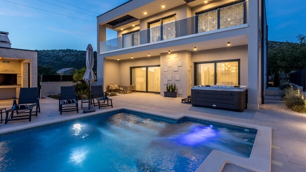 Een modern huis met twee verdiepingen, een zwembad, buitenmeubilair en een jacuzzi.