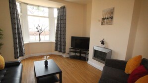A living room with a sofa, a coffee table, a TV, and a fireplace. - Lundwood House (Barnsley)