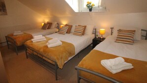 A hotel room with two beds, each with a brown blanket and white pillows. There is a window with a view of the outside, and a nightstand with a lamp between the beds. - Lundwood House (Barnsley)