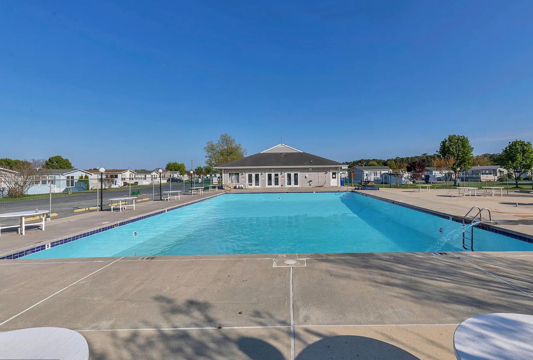 Une piscine rectangulaire avec une zone de terrasse carrelée à l’avant, le tout entouré d’une clôture.