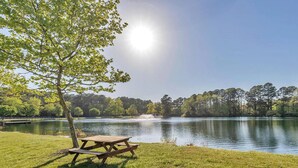 A lakeside picnic area with a wooden table and benches, surrounded by lush greenery and trees. - Comfortable cottage in gated community, 5 mins to OC and Assateague (Berlin)