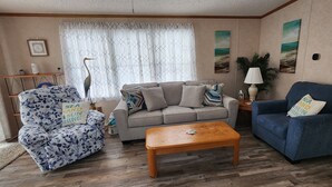 A living room with a grey sofa, a blue armchair, and a patterned armchair. There is a wooden coffee table in the center. - Comfortable cottage in gated community, 5 mins to OC and Assateague (Berlin)