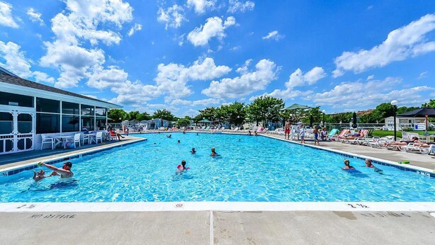 A large outdoor swimming pool with people swimming and lounging, surrounded by a fence and shaded areas. - Comfortable cottage in gated community, 5 mins to OC and Assateague (Berlin)