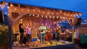 Eine rustikale Freilichtbühne mit Holzkonstruktion, Lichterketten und Musikinstrumenten.