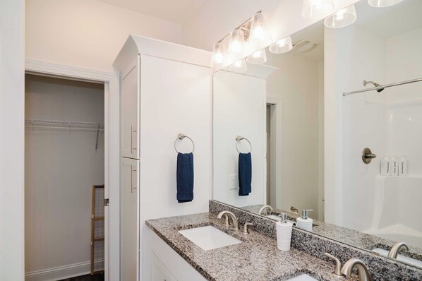 A bathroom with a granite countertop, two sinks, a large mirror, and a shower area. - Spacious Beach Stay w/ Pool, Spa, Views & Kings! (North Topsail Beach)