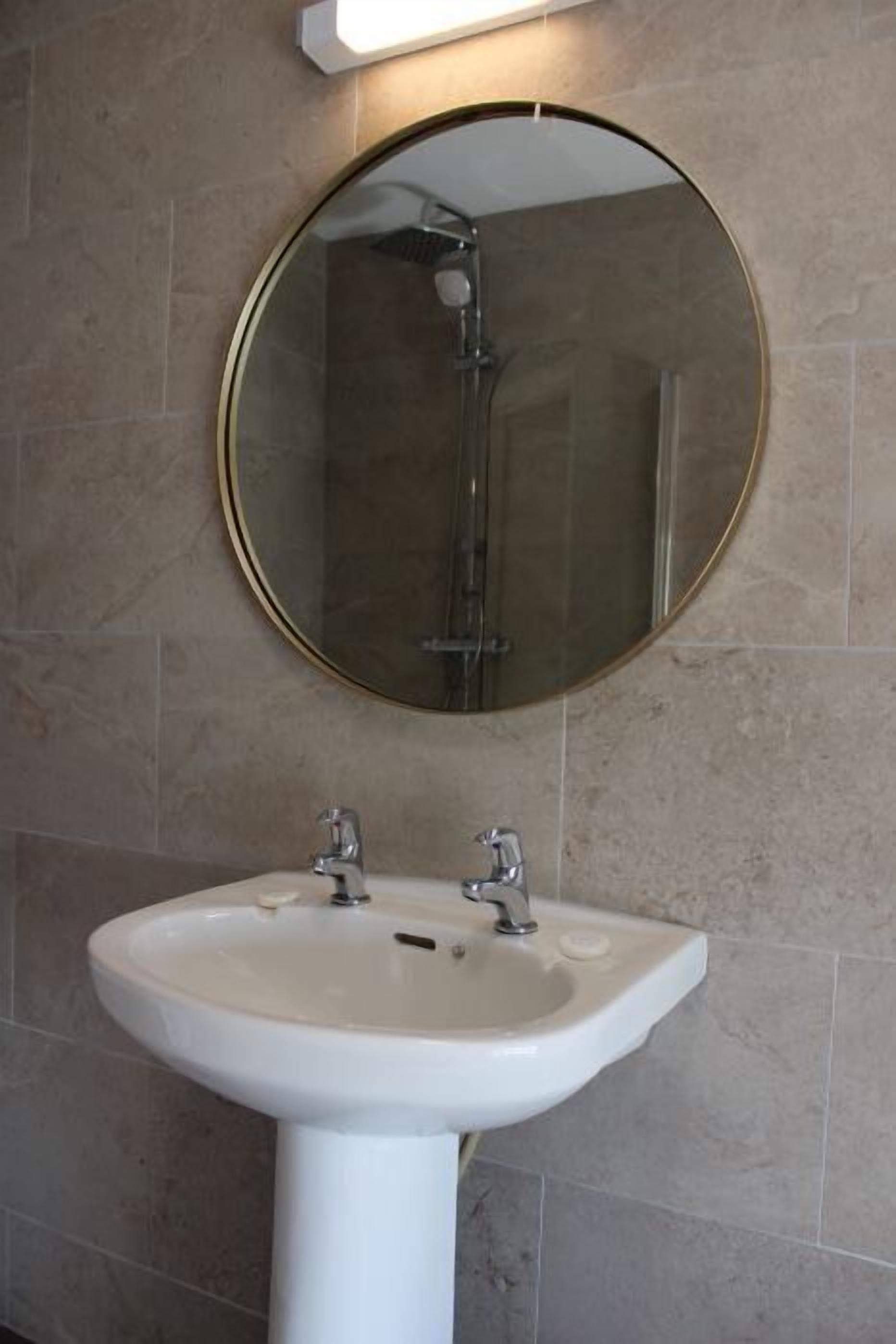 Une salle de bain avec un miroir rond, un lavabo blanc et une douche.
