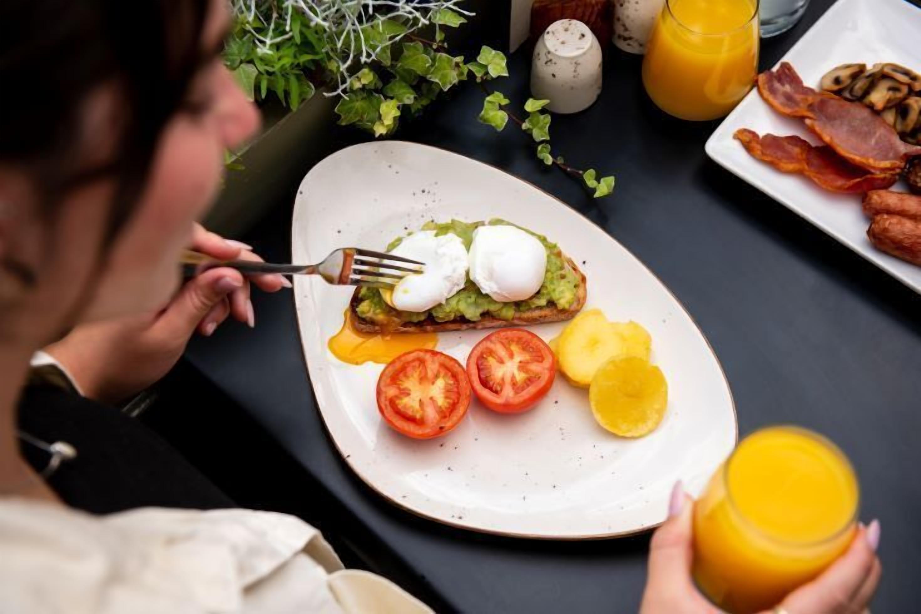 Un plato de desayuno con huevos, aguacate, tomates y rodajas de limón.