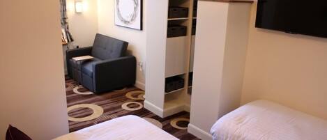 A hotel room with two beds, a wardrobe, a TV, and a seating area with a couch and a chair.
