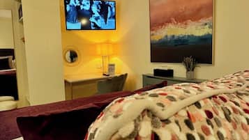 A hotel room with a bed, a television mounted on the wall, and a painting above the bed.