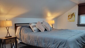 Un dormitorio con cama, dos mesitas de noche, una ventana y una lámpara en el techo.