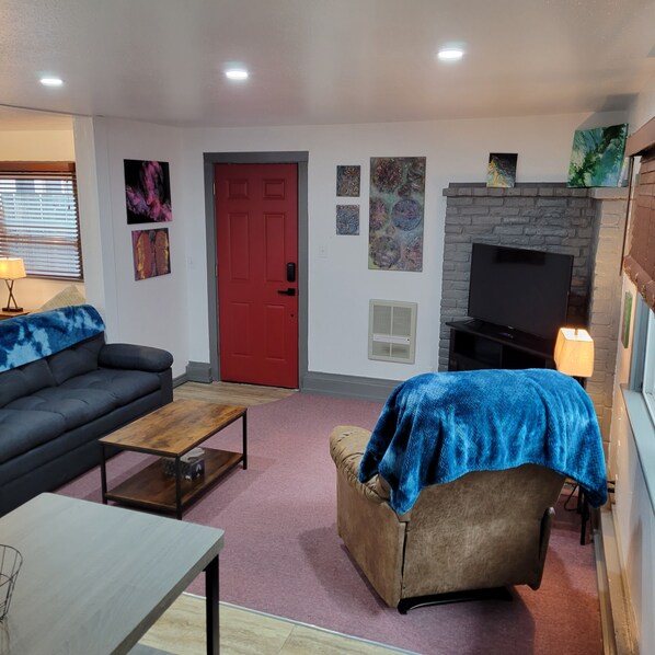 Ein Wohnzimmer mit roter Tür, einer Couch, einem Couchtisch, einem Fernseher und einem Kamin.