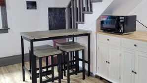 Una cocina con una mesa de madera y taburetes, un microondas y armarios blancos.