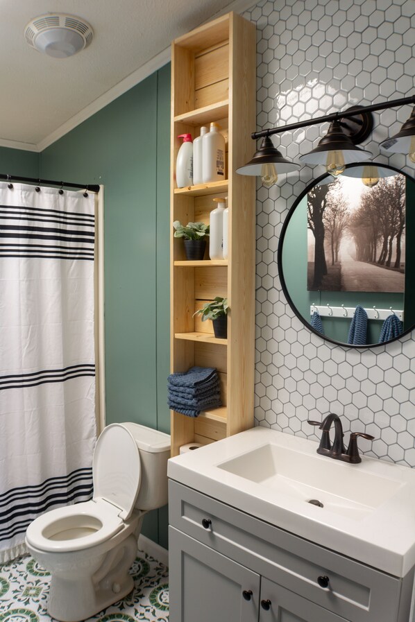 Une salle de bain équipée de toilettes, d’un lavabo, d’un miroir et d’une étagère contenant des articles de toilette.