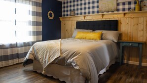 A bedroom with a checkered wall, a bed with a headboard, a bedside table, and a window with curtains. - Family friendly bungalow with big yard and deck, close to town (Deckerville)