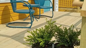 A yellow building with a blue door and a 'WELCOME' sign, a wooden deck with two blue chairs, and three potted plants. - Family friendly bungalow with big yard and deck, close to town (Deckerville)