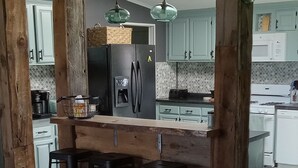 A spacious kitchen with wooden beams, a central island with stools, and modern appliances. - Family friendly bungalow with big yard and deck, close to town (Deckerville)