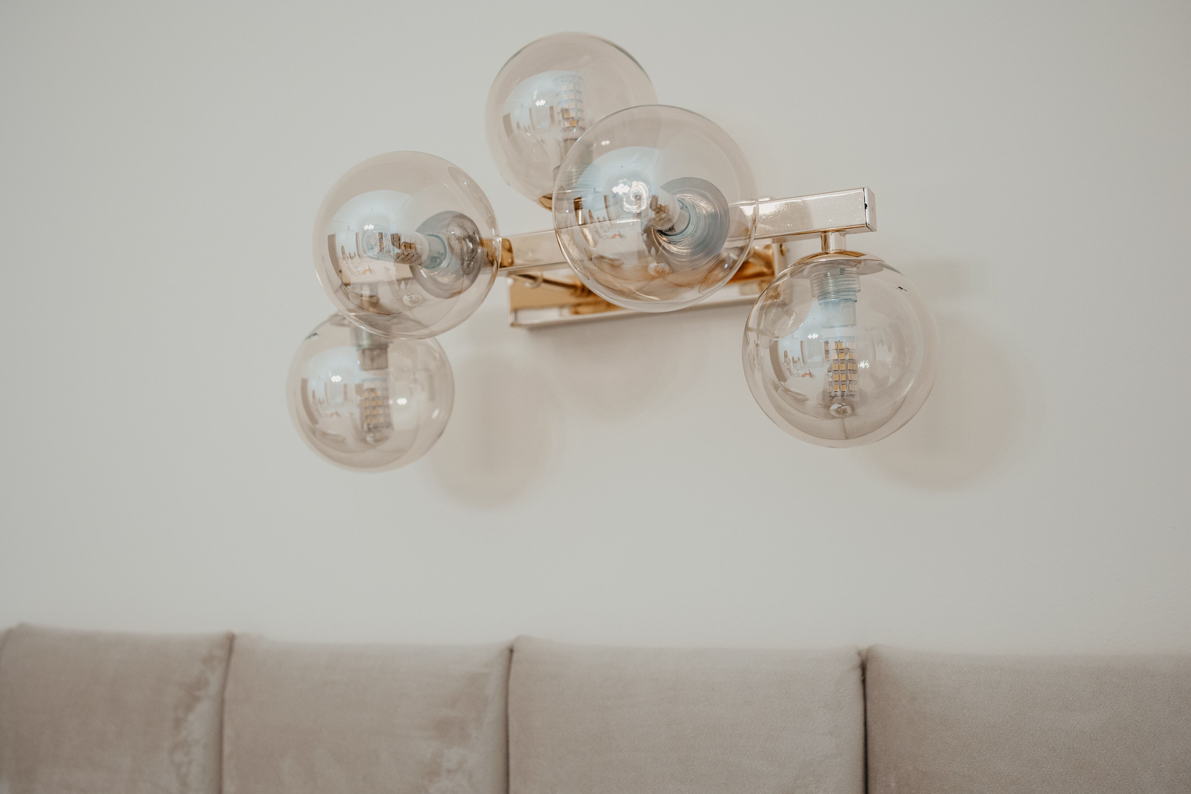 A wall-mounted light fixture with four clear glass globes and a gold-colored metal structure.