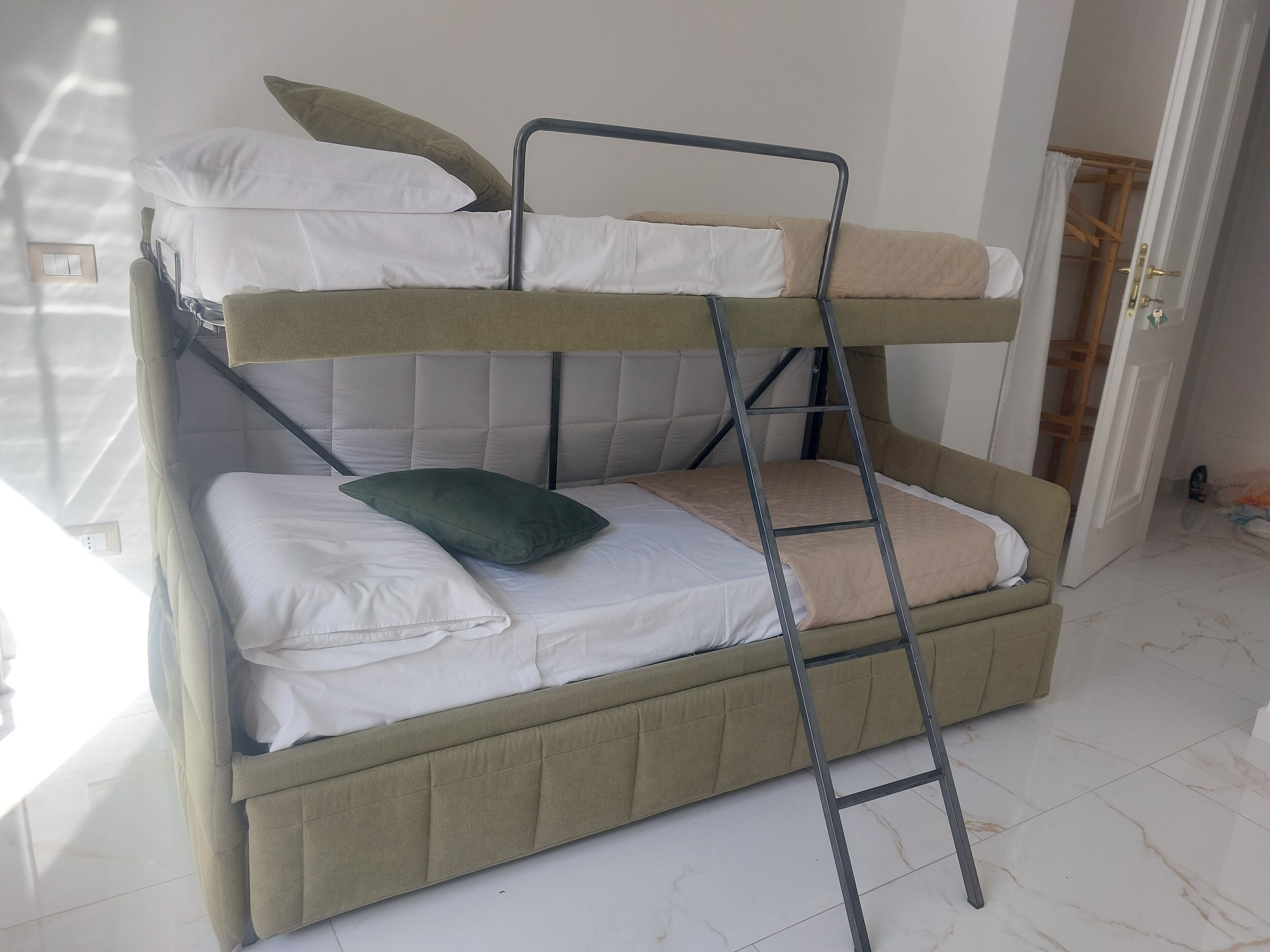 Un lit superposé avec une échelle, une literie blanche et beige, et une porte en bois en arrière-plan.
