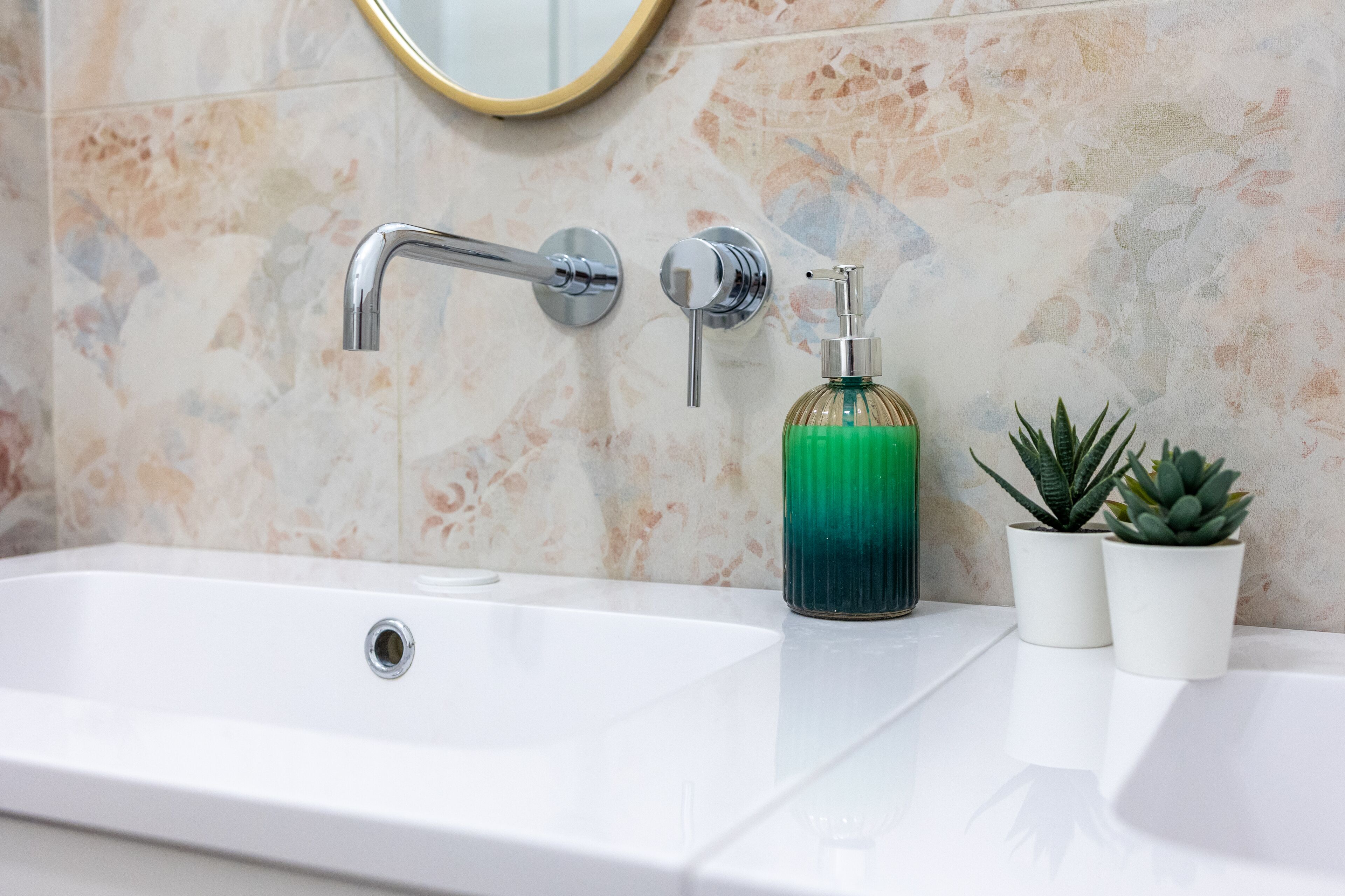 A bathroom with a white sink, a chrome faucet, a soap dispenser, and two potted plants.
