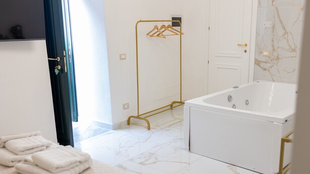 A modern bathroom with a white bathtub, a gold towel rack, and a neatly folded set of towels on the floor. - Borgo La Chiusa (Cinisi)