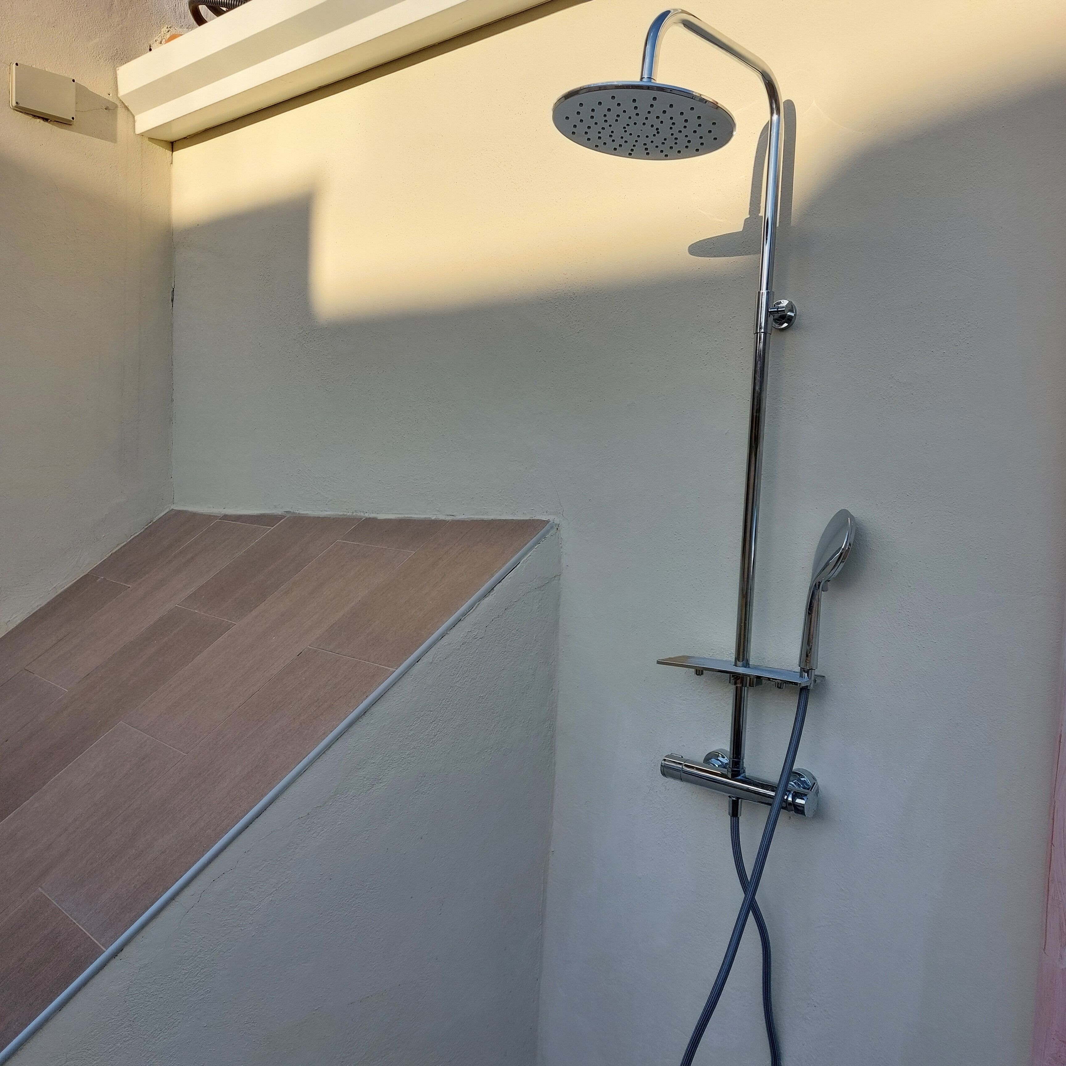 A shower area with a handheld showerhead, a wall-mounted faucet, and a flexible hose.