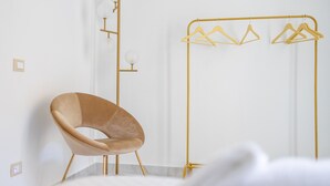 A modern room with a minimalist design, featuring a unique curved chair, a gold-colored clothing rack, and a simple light fixture. - Borgo La Chiusa (Cinisi)