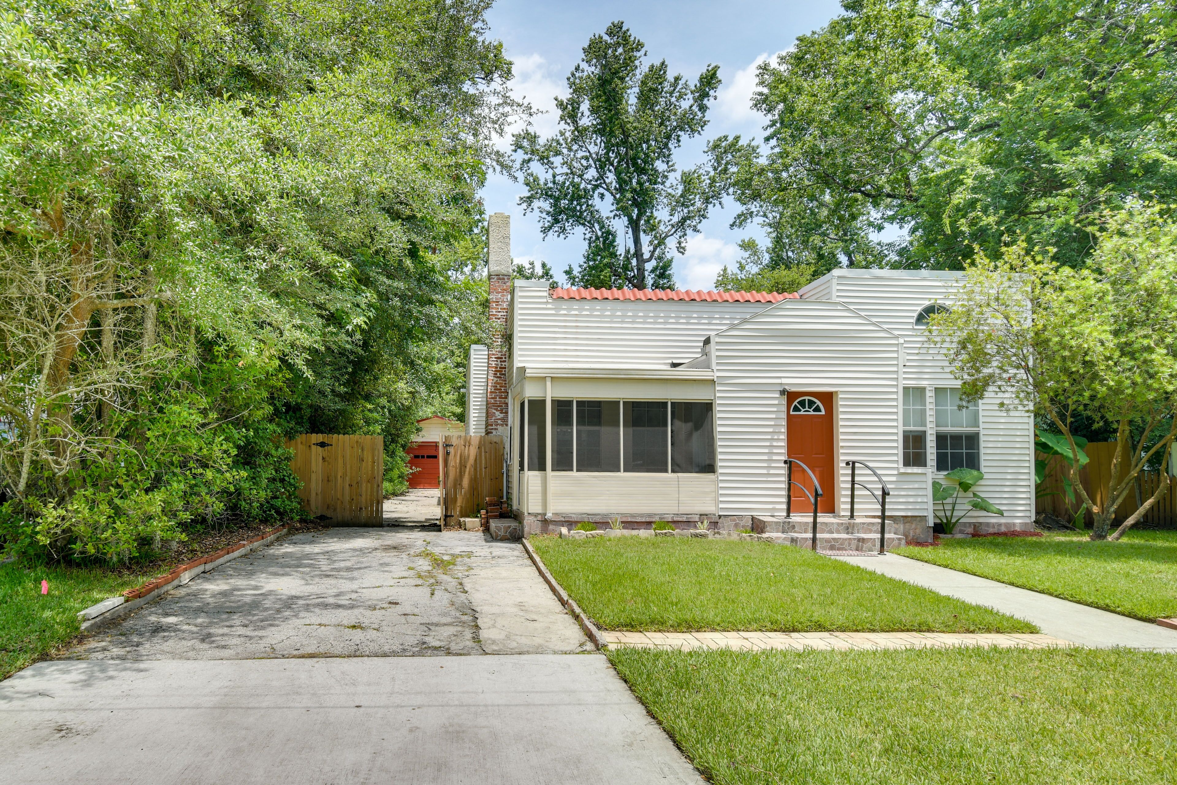 A single-story house with a red door, a small front yard, and a wooden fence.