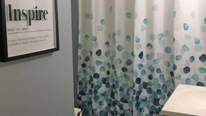 Un baño con una cita inspiradora enmarcada en la pared, un inodoro y una cortina de ducha con estampado de lunares azules y blancos.
