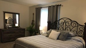 Un dormitorio con cama, cómoda, guitarra y espejo.