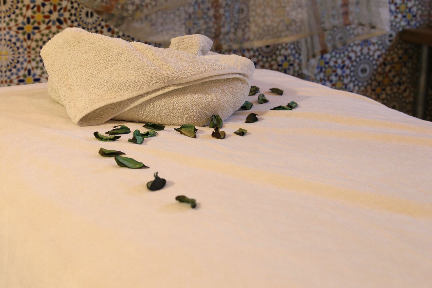 A neatly folded white towel on a bed with a patterned tile floor.