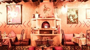 Un coin repas chaleureux avec une cheminée, une table dressée pour deux personnes et un mur décoré d’œuvres d’art.
