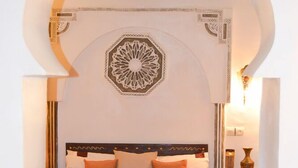 Un lit recouvert d’une couverture à motifs, une décoration murale et une table de chevet avec une lampe.