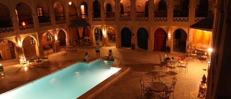 Un patio con piscina, mobiliario exterior y puertas abovedadas.