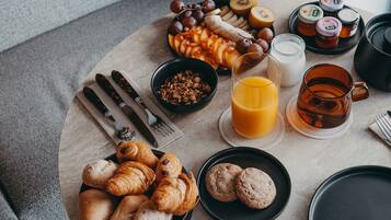 A breakfast setting with croissants, cookies, fruits, honey, and a coffee mug on a round table.