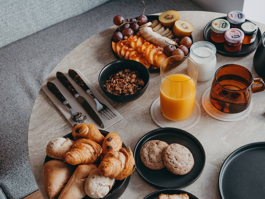 A breakfast setting with croissants, cookies, fruits, honey, and a coffee mug on a round table.