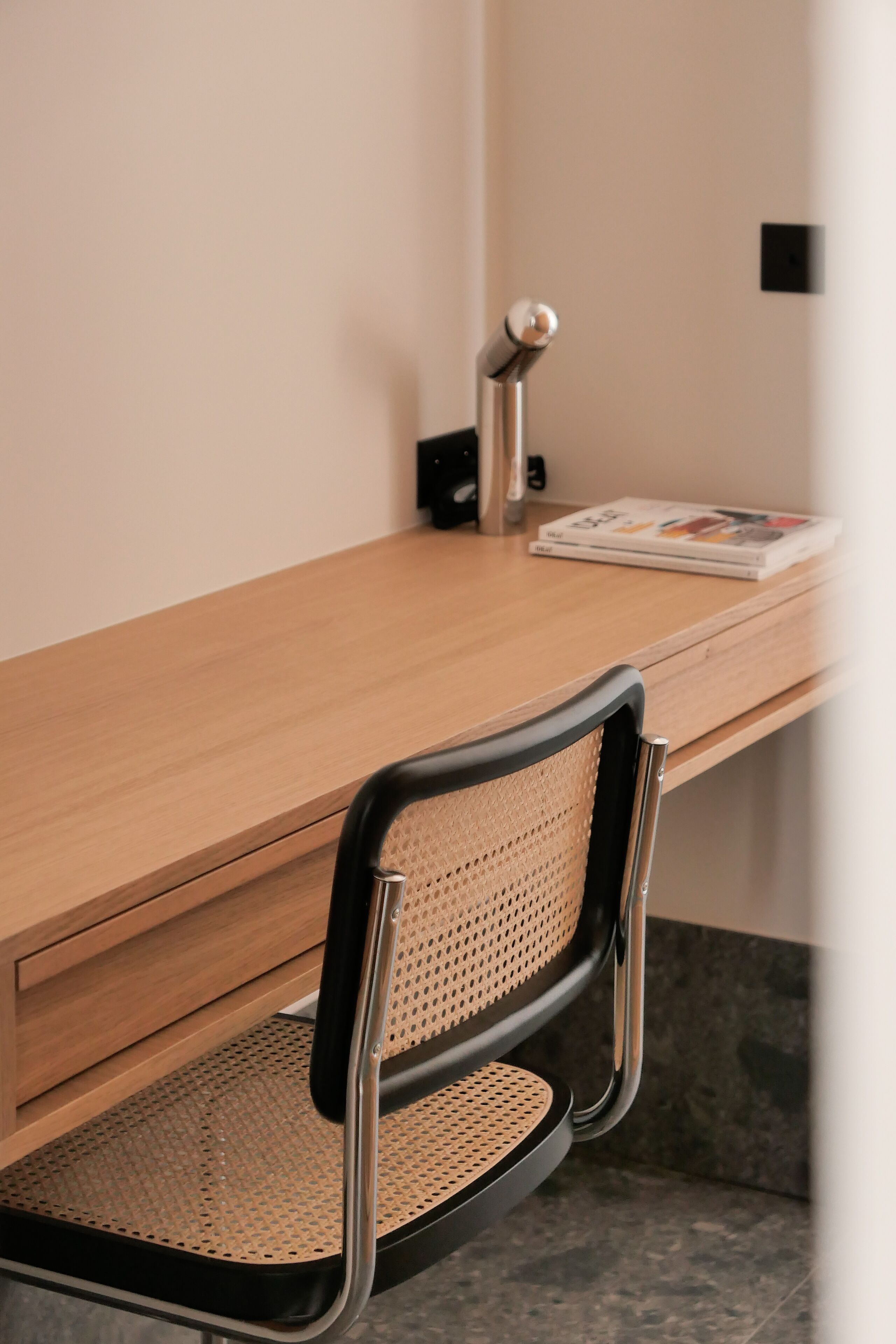 A wooden desk with a black chair that has a woven backrest.