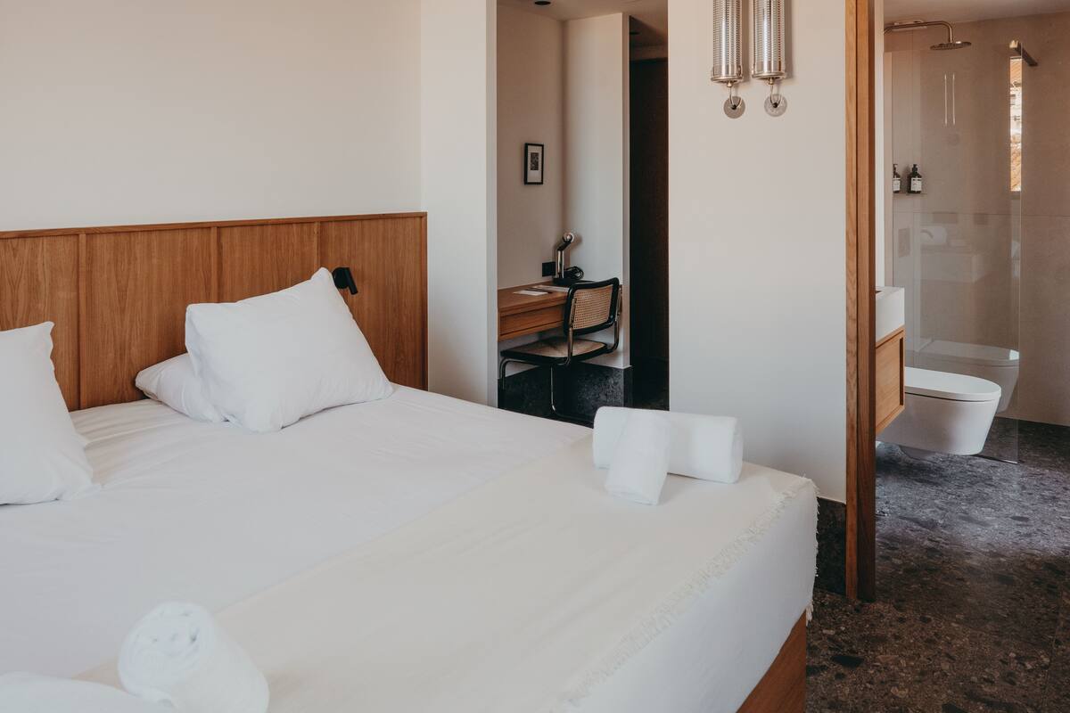 A hotel room with a wooden headboard, a desk with a chair, a bathroom with a shower, and a toilet.