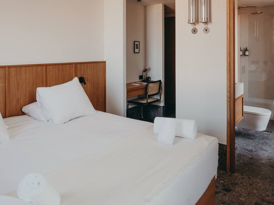Habitación de hotel con cabecera de madera, un escritorio con silla, baño con ducha y retrete.