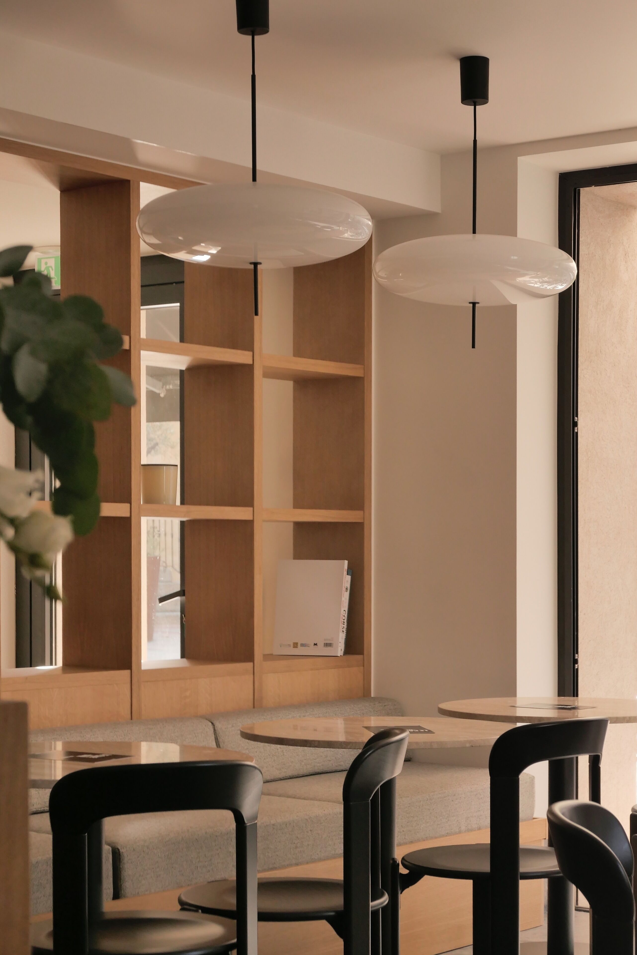 Un intérieur moderne avec une table ronde, des chaises noires, une bibliothèque en bois et des luminaires suspendus.
