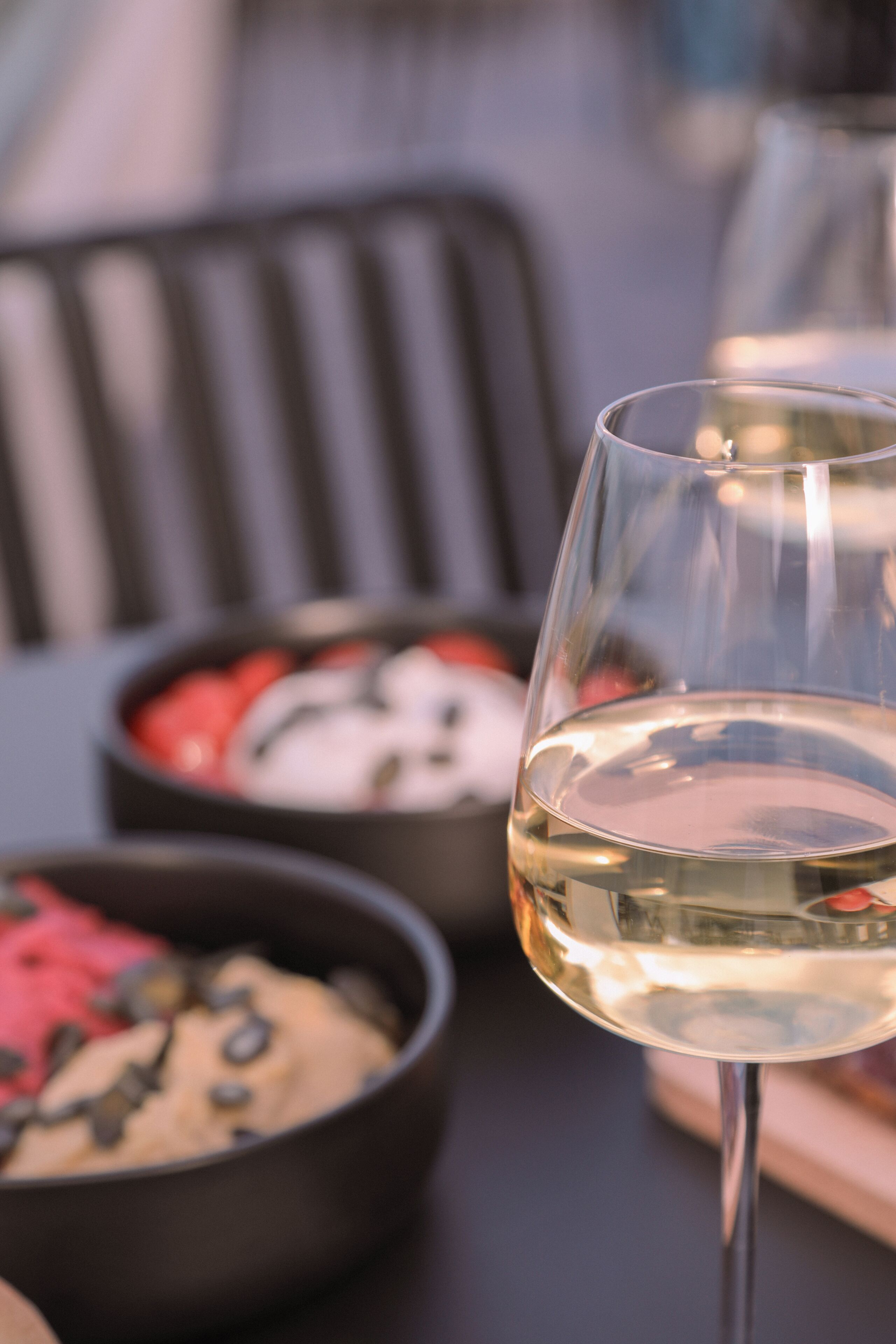A glass of white wine on a table with two bowls of food in the background.