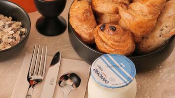 Een tafel met croissants, een potje Danone yoghurt en een kaars.