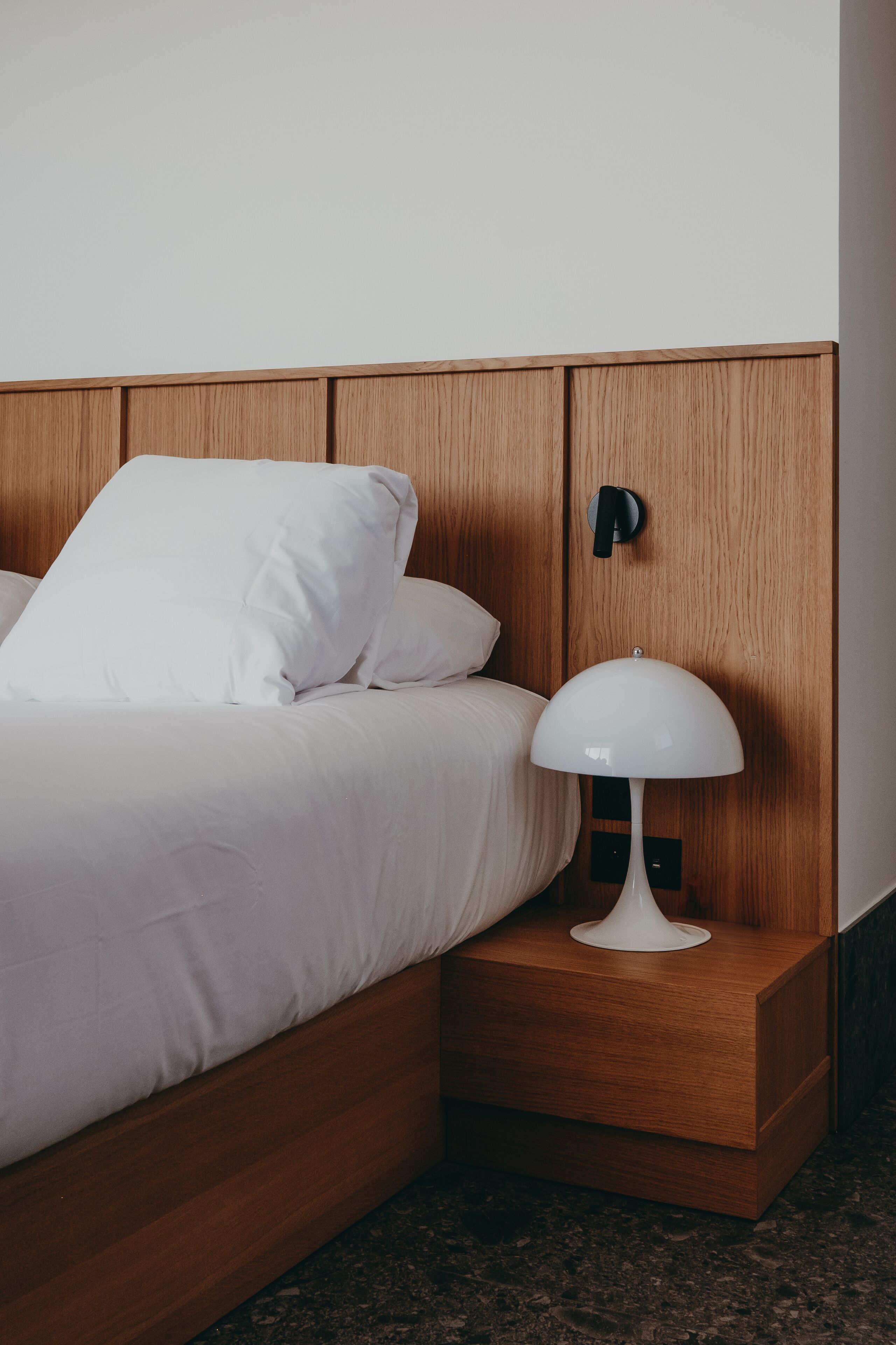 A neatly made bed with white linens, a wooden headboard, and a bedside table with a white lamp.