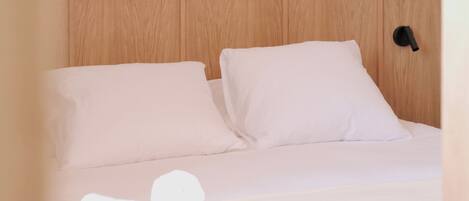 Una cama bien hecha con sábanas blancas, un cabecero de madera y un objeto negro en la pared.