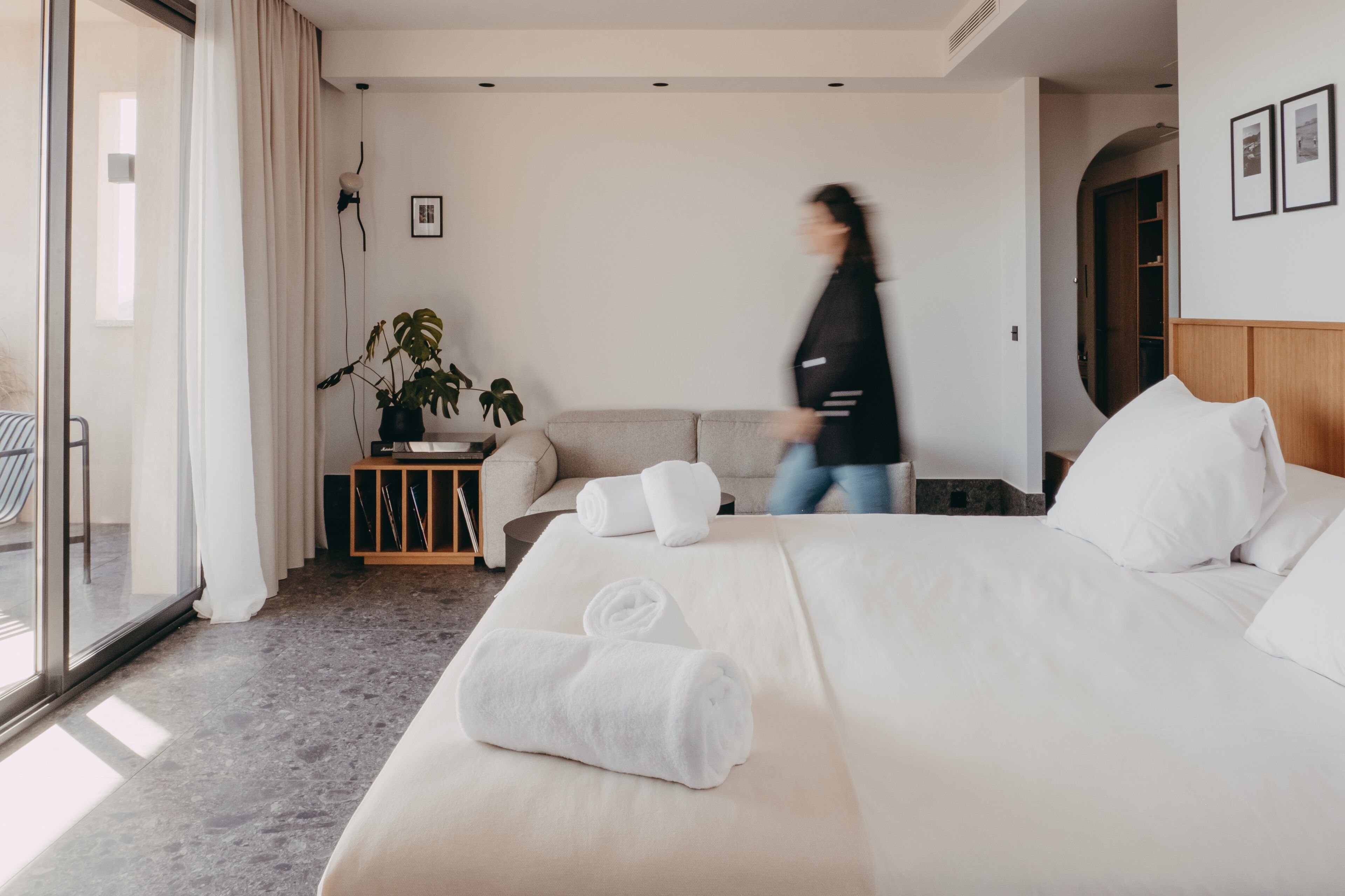 Habitación de hotel con una cama grande, una mesita de noche con una planta y vistas a través de una puerta corredera.
