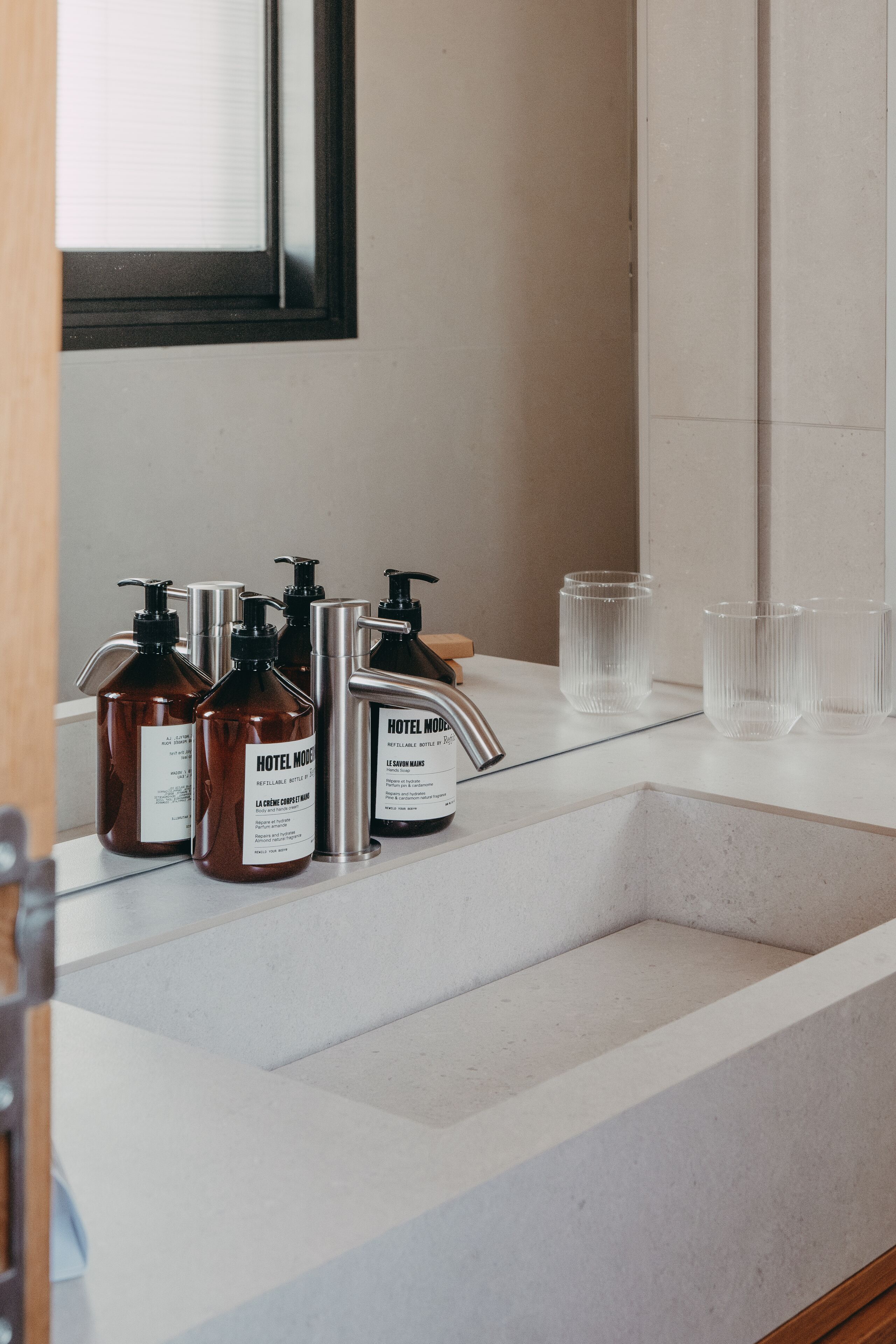 A bathroom sink with Hotel Mode toiletries and clear glasses on the counter.