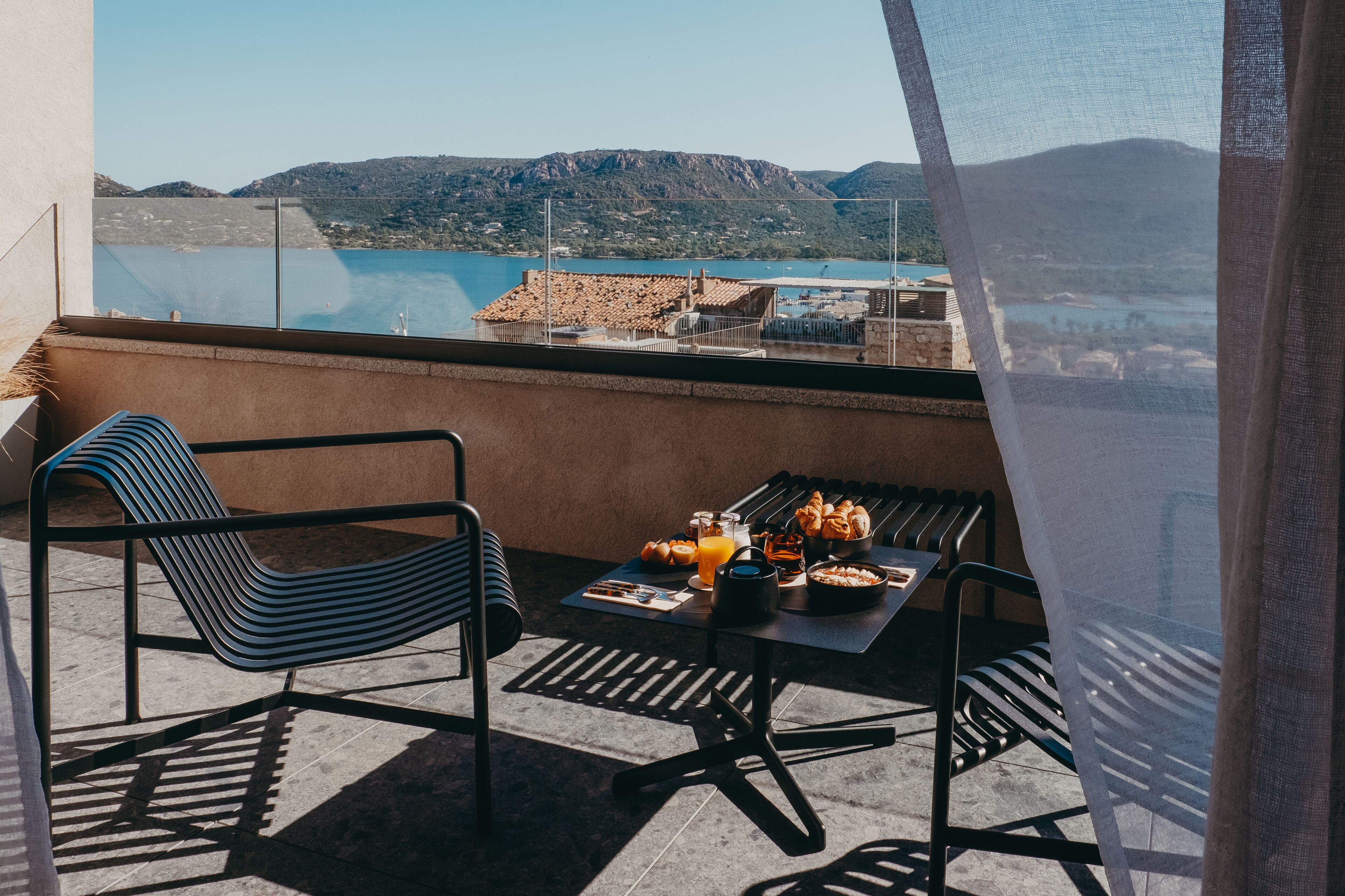 Un balcon avec une table préparée pour le petit-déjeuner, une chaise et une vue sur un lac et des montagnes.