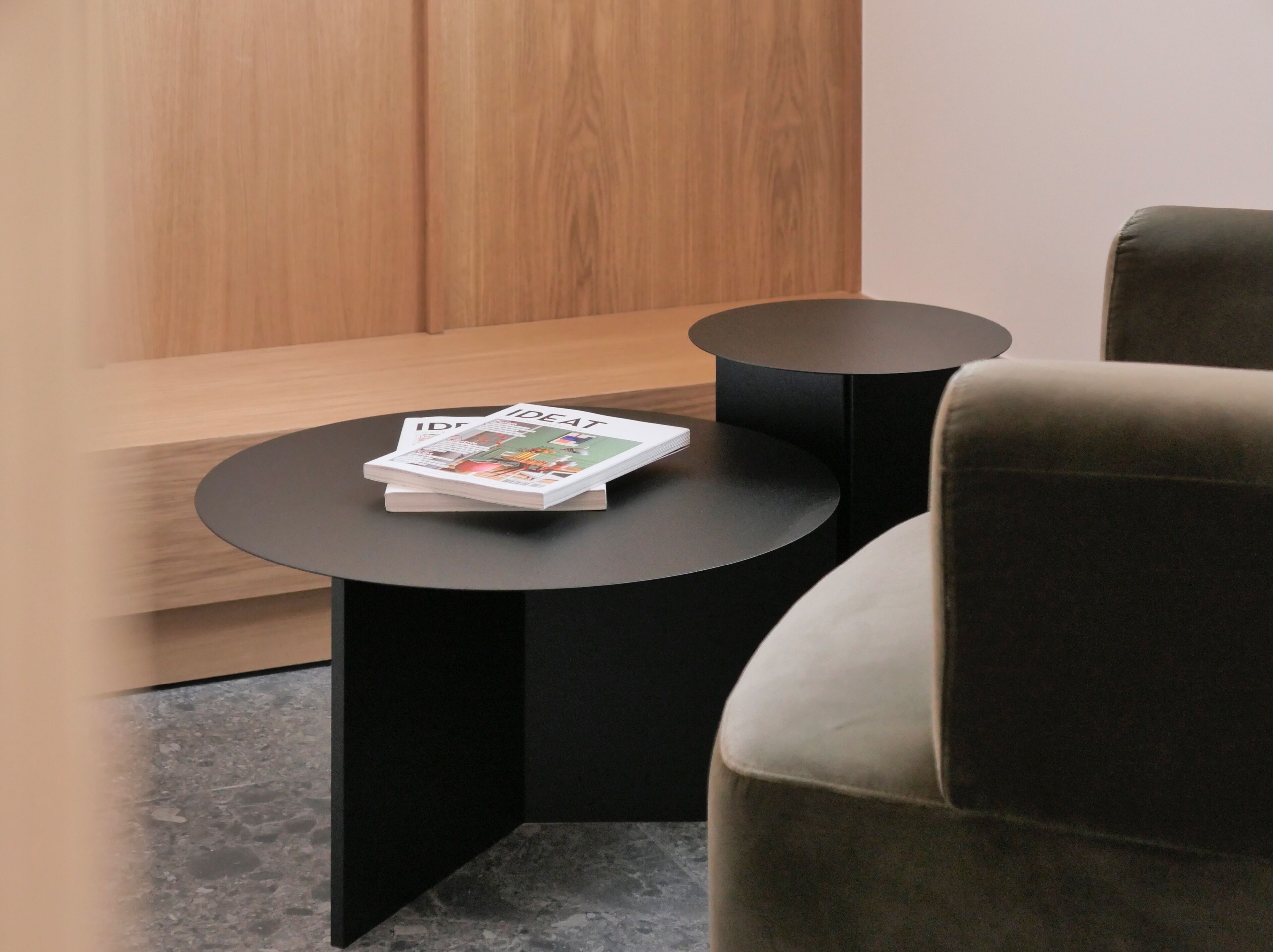 A modern room with a wooden panel wall, a black round table with a magazine, and a grey upholstered chair.