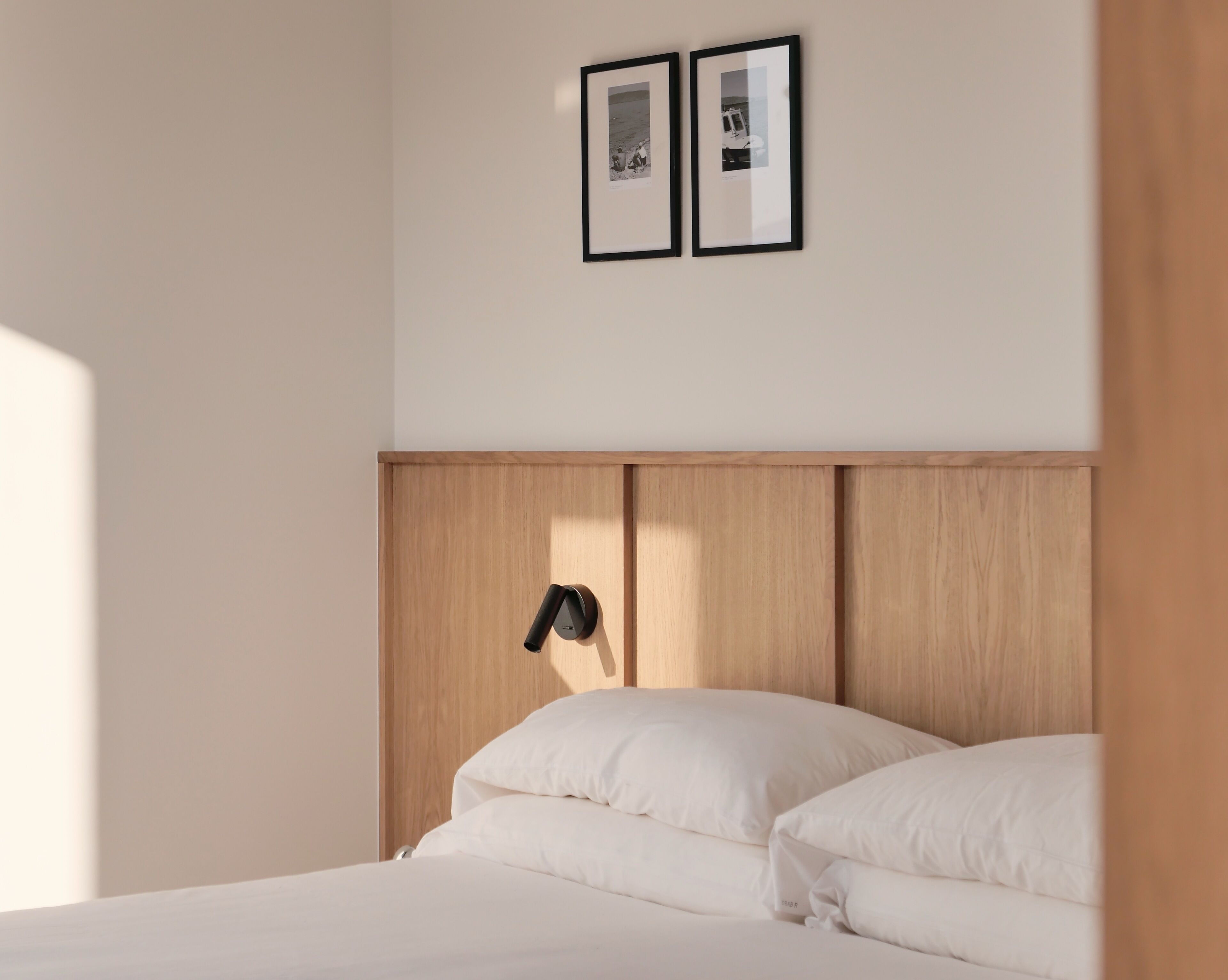 A bedroom with a wooden headboard, a bedside table with a lamp, and two framed pictures on the wall.