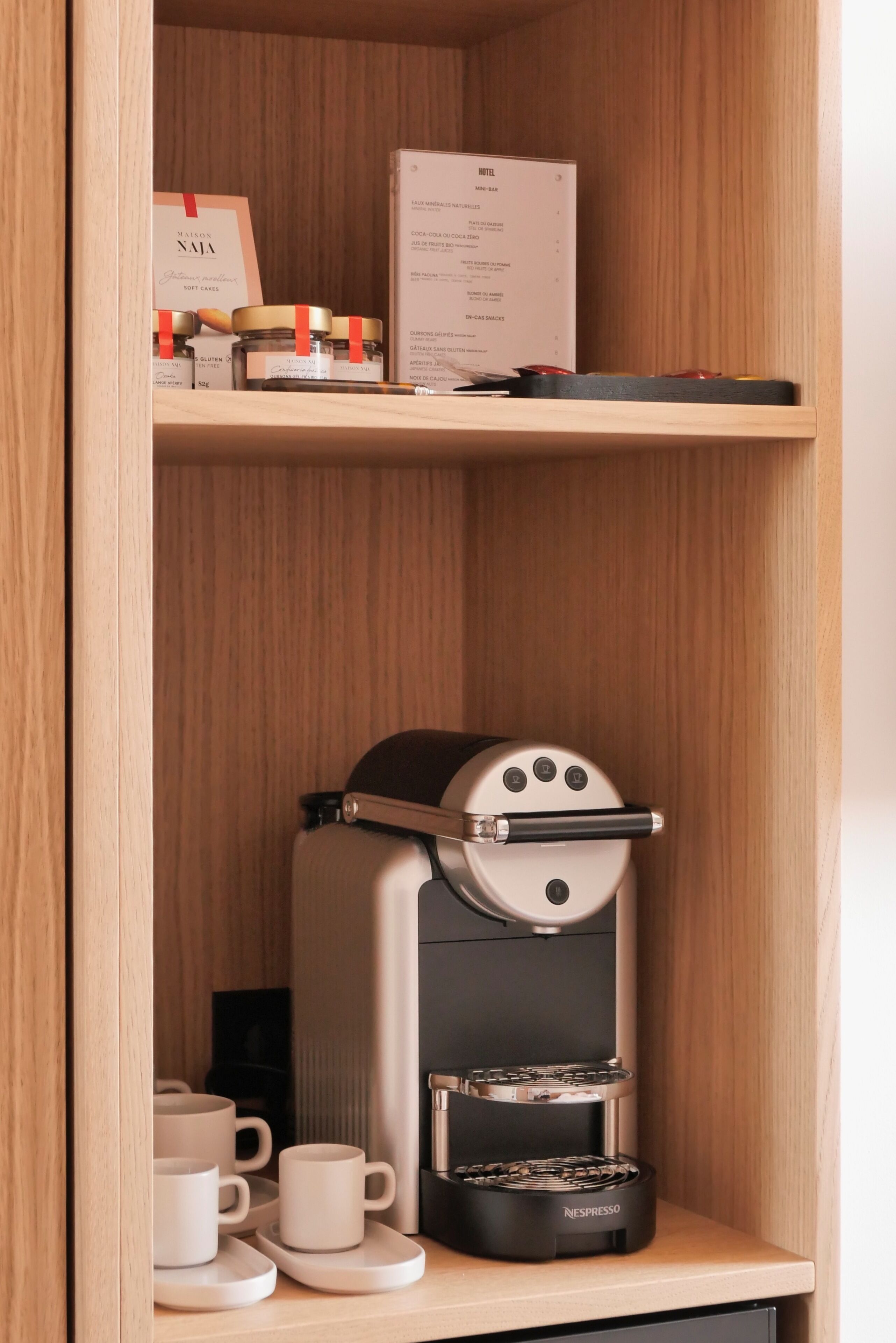 Una cafetera Nespresso en un mueble de madera con un menú y frascos de pastel suave en el estante superior.